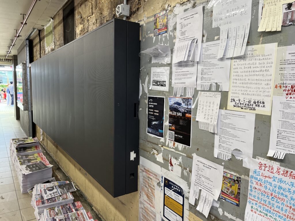 Sunnybank墙另一端，LED屏全貌，食阁倒影映在烧腊窗，墙根报纸堆
