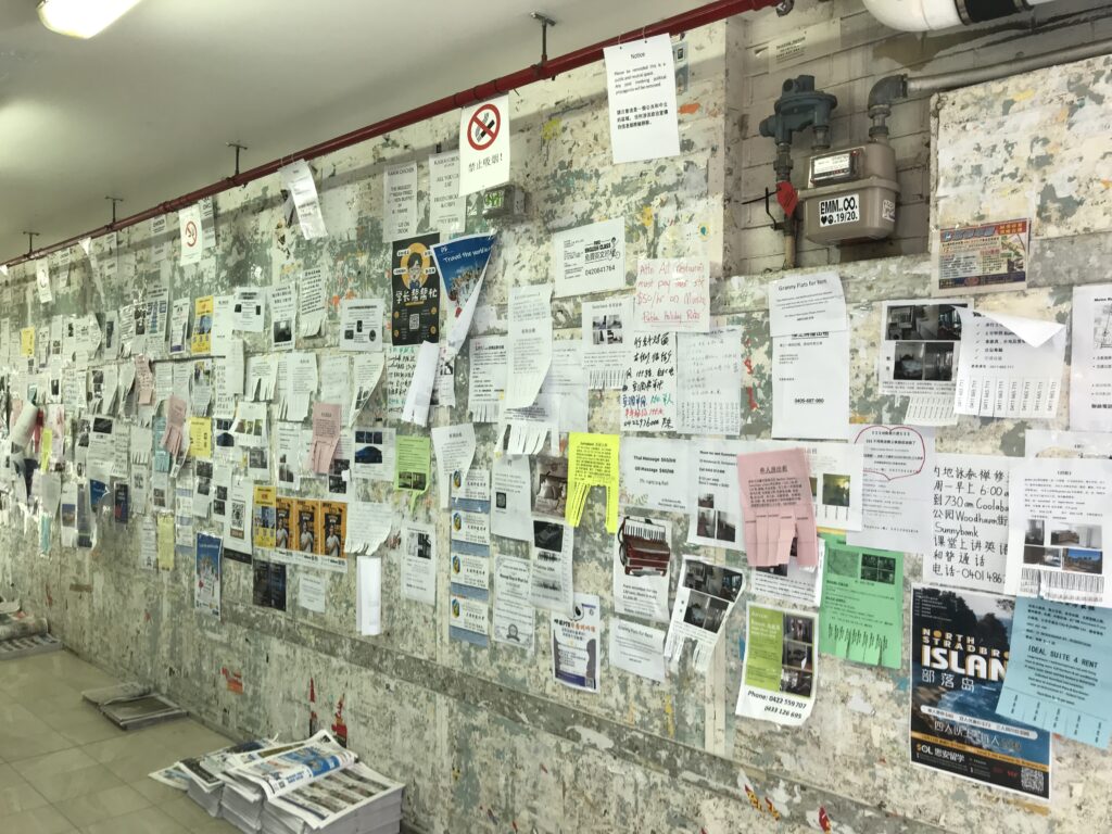 Sunnybank墙另一端，红色消防管横跨天花，电表箱在右，墙面传单层叠