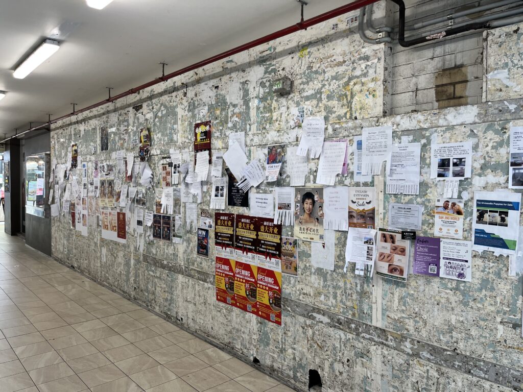 Sunnybank灰色公告墙，角度拍摄，层层叠叠的彩色海报和传单