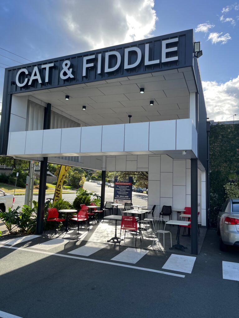 Cat & Fiddle村白色灰色方形用餐舱，下午阳光，桌椅，绿色花园，停车位，屋顶CAT & FIDDLE字样