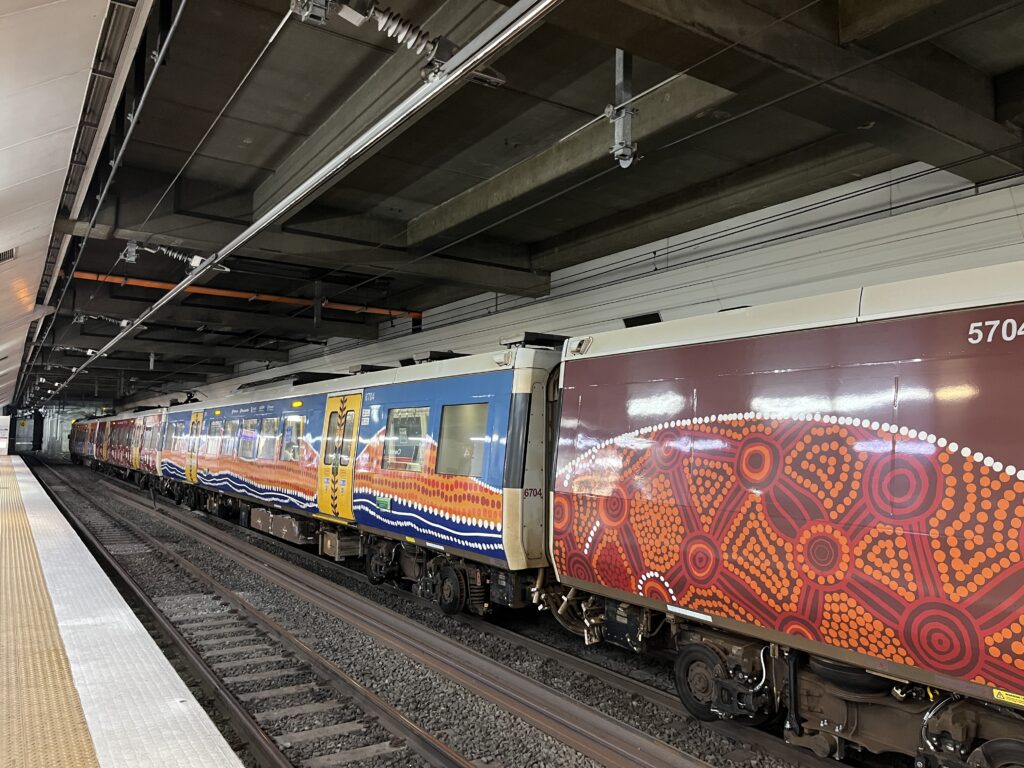 中央车站站台，火车停靠副轨，车身原住民艺术棕红橙图案，代表沙漠内陆与水潭