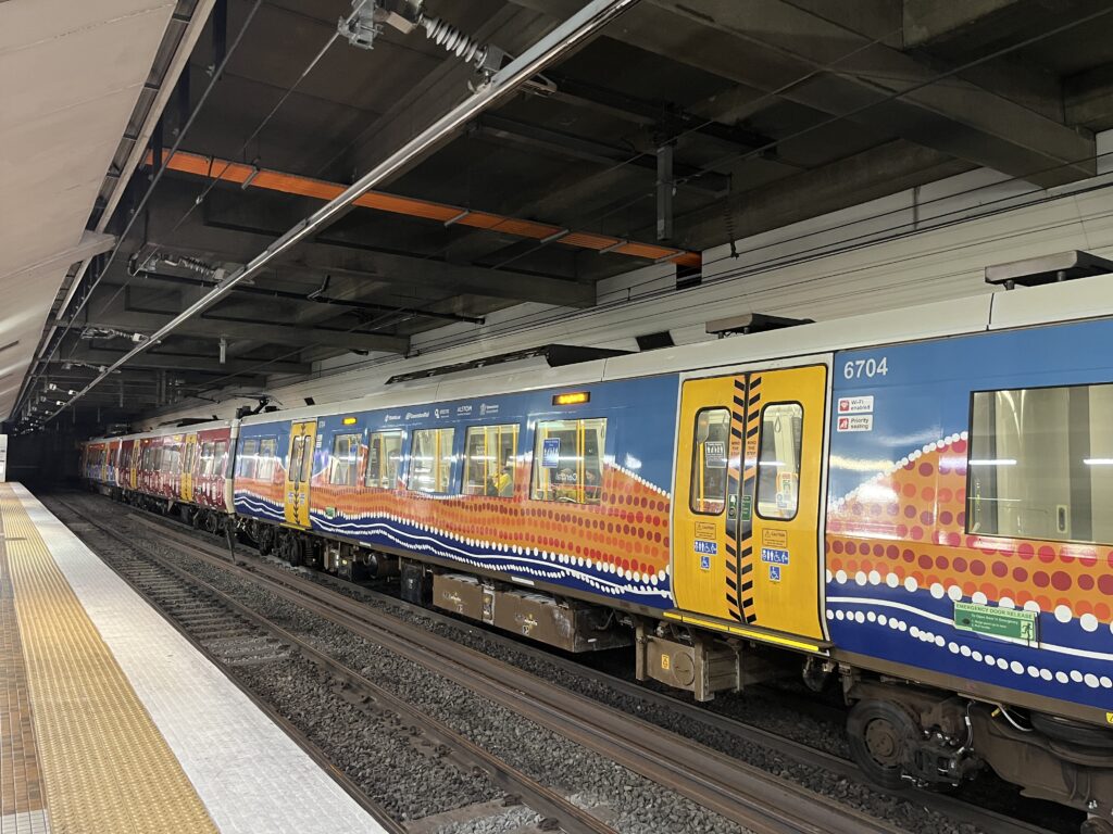 中央车站站台，火车停靠副轨，车身原住民艺术蓝橙黄图案，代表海与陆地