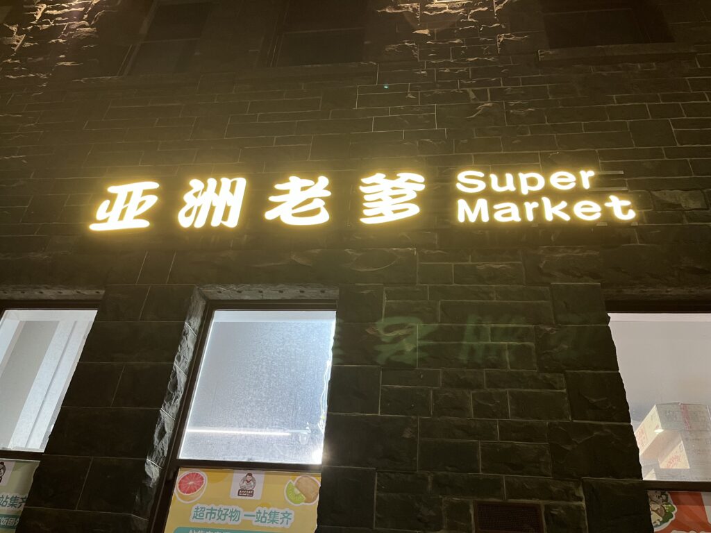 墨尔本深夜亚洲超市，灰色砖墙，中文霓虹招牌，食品广告贴窗