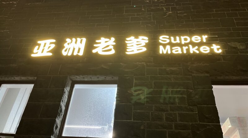 墨尔本深夜亚洲超市，灰色砖墙，中文霓虹招牌，食品广告贴窗