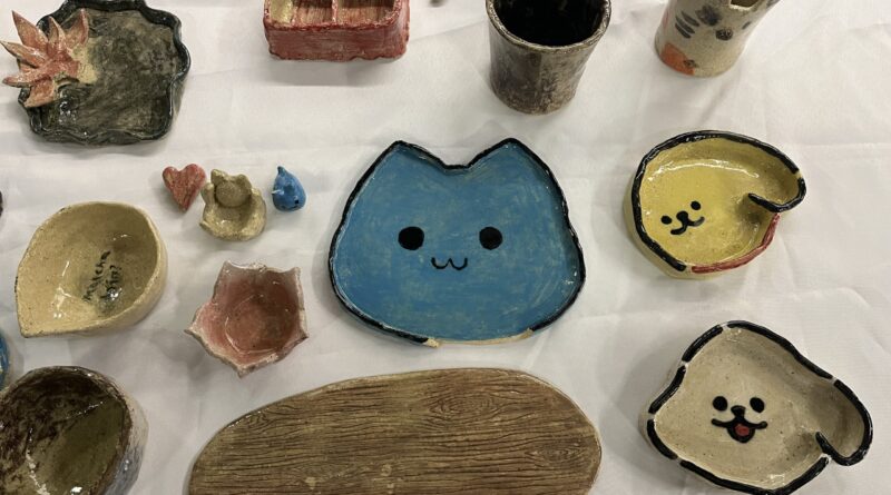 学生手工陶艺作品，白桌布上摆满盘碟杯碗，蓝猫黄狗绿荷叶盘