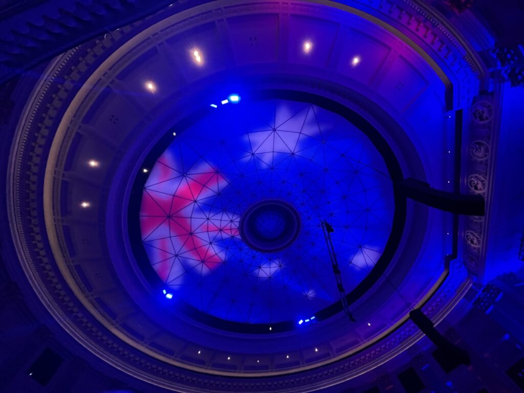 布里斯班市政厅礼堂穹顶天花板，中央玻璃采光板，环形纹路，澳洲国旗投影，蓝紫色灯光，红白蓝配色