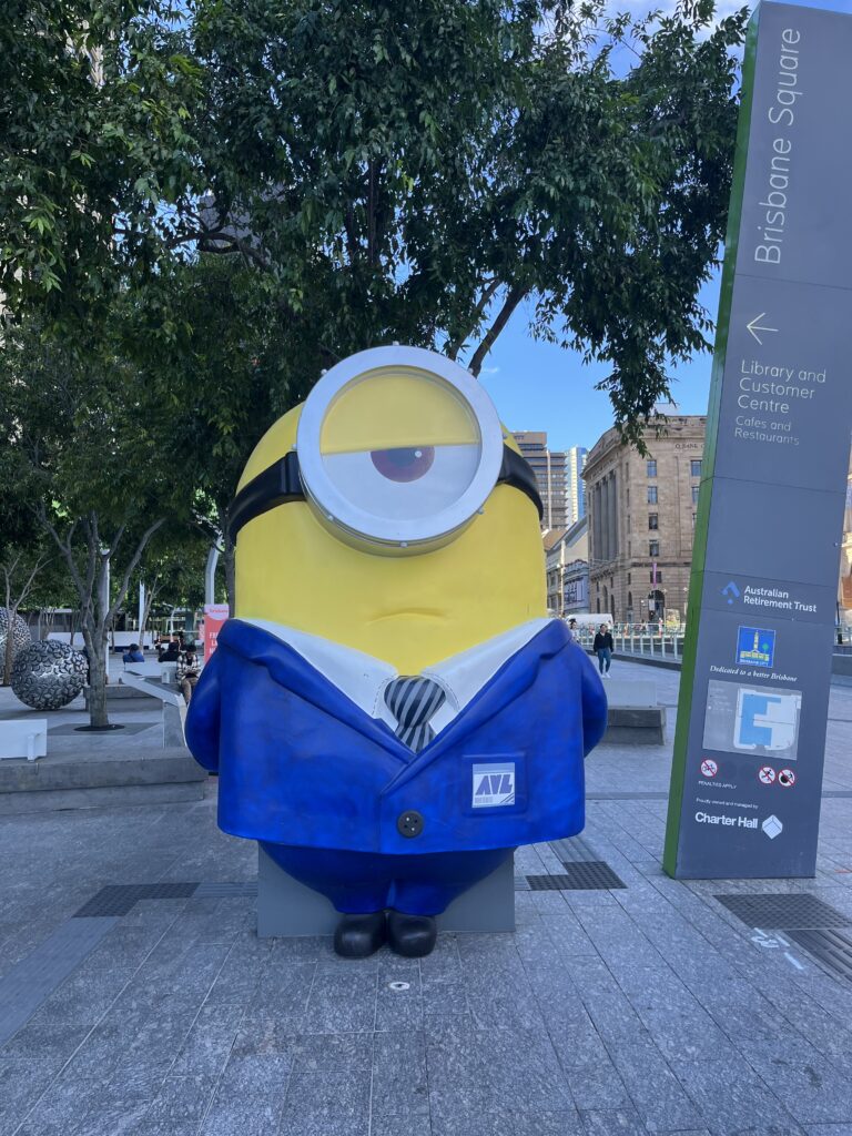 布里斯班广场，路标指向布里斯班市立图书馆，蓝色小黄人单手背后思考表情