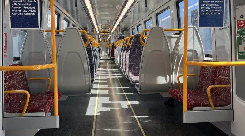 布里斯班火车车厢内景，对称构图，中央走道，两侧座椅，天花板两排灯，红黄蓝白配色