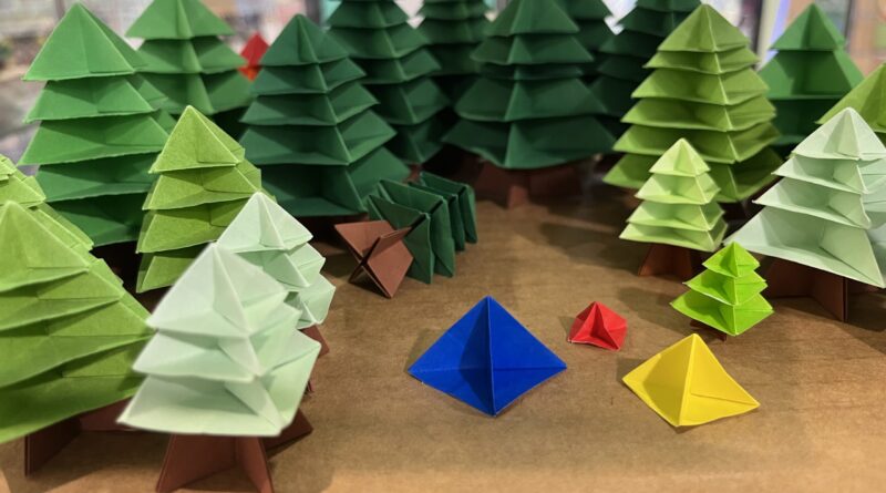 折纸森林展览，彩色圣诞树状纸树排列，空地中有蓝红黄三角形纸模型如帐篷