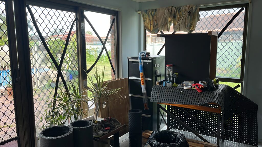 气旋过后第二天，阳光房角落，玻璃完好，家具仍抵在窗前，室外更亮