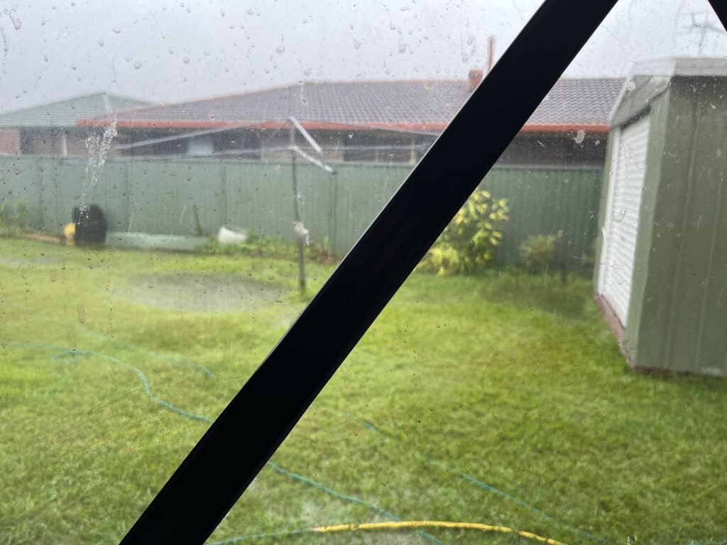 气旋前窗外后院，胶带斜贴玻璃，草坪积水，灰色阴天