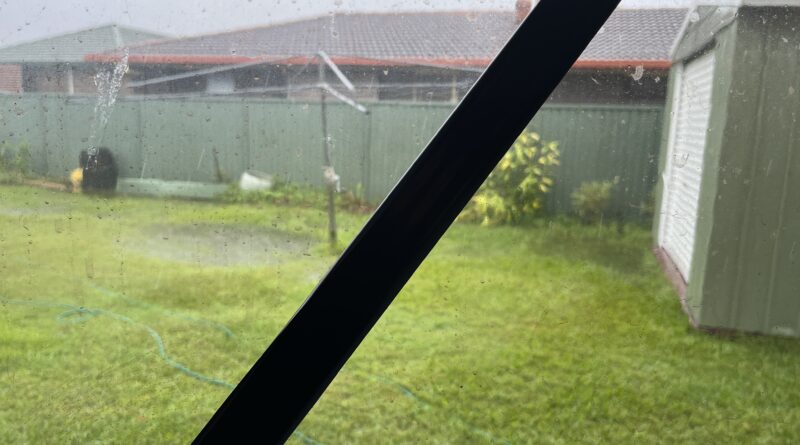 气旋前窗外后院，胶带斜贴玻璃，草坪积水，灰色阴天