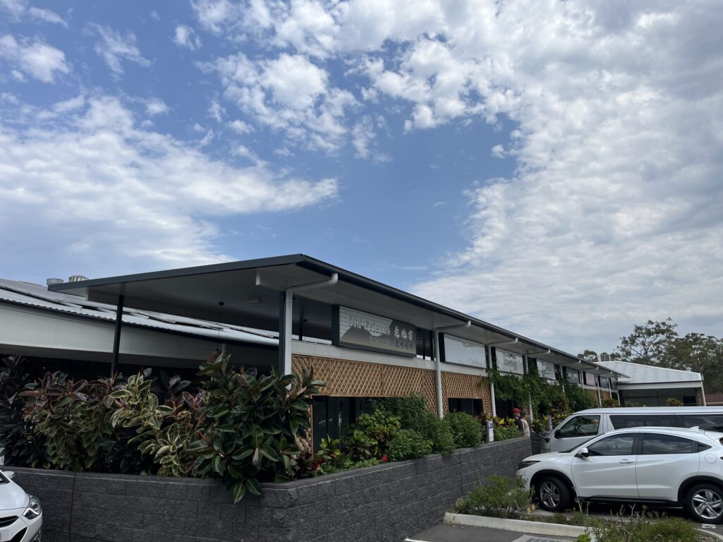 罗伯逊村户外用餐区，灰色砖墙，绿色植物，木格栅，悬吊植物，蓝天白云