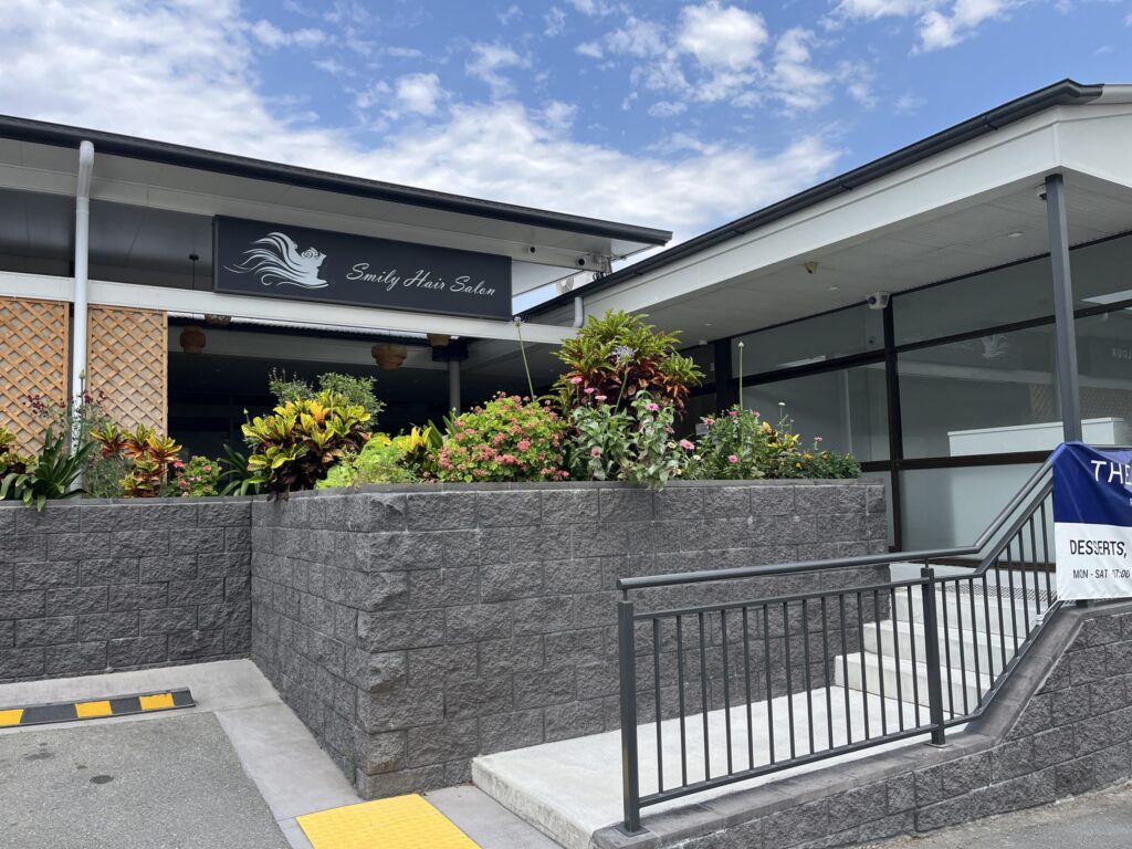 罗伯逊村灰色挡土墙，上方种植床，右侧短楼梯带扶手通向店铺，角落店铺空置，上方悬挂花盆或灯笼