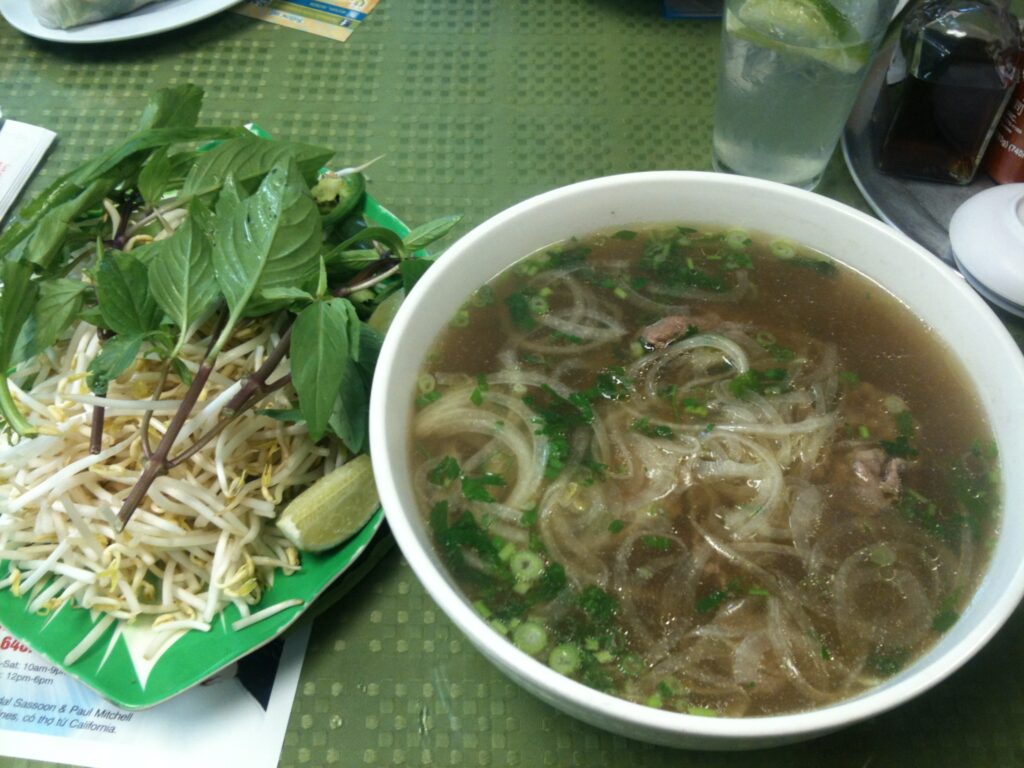 绿色桌面中央一碗越南牛肉粉，右侧豆芽薄荷柠檬碟，上方部分饮品小料