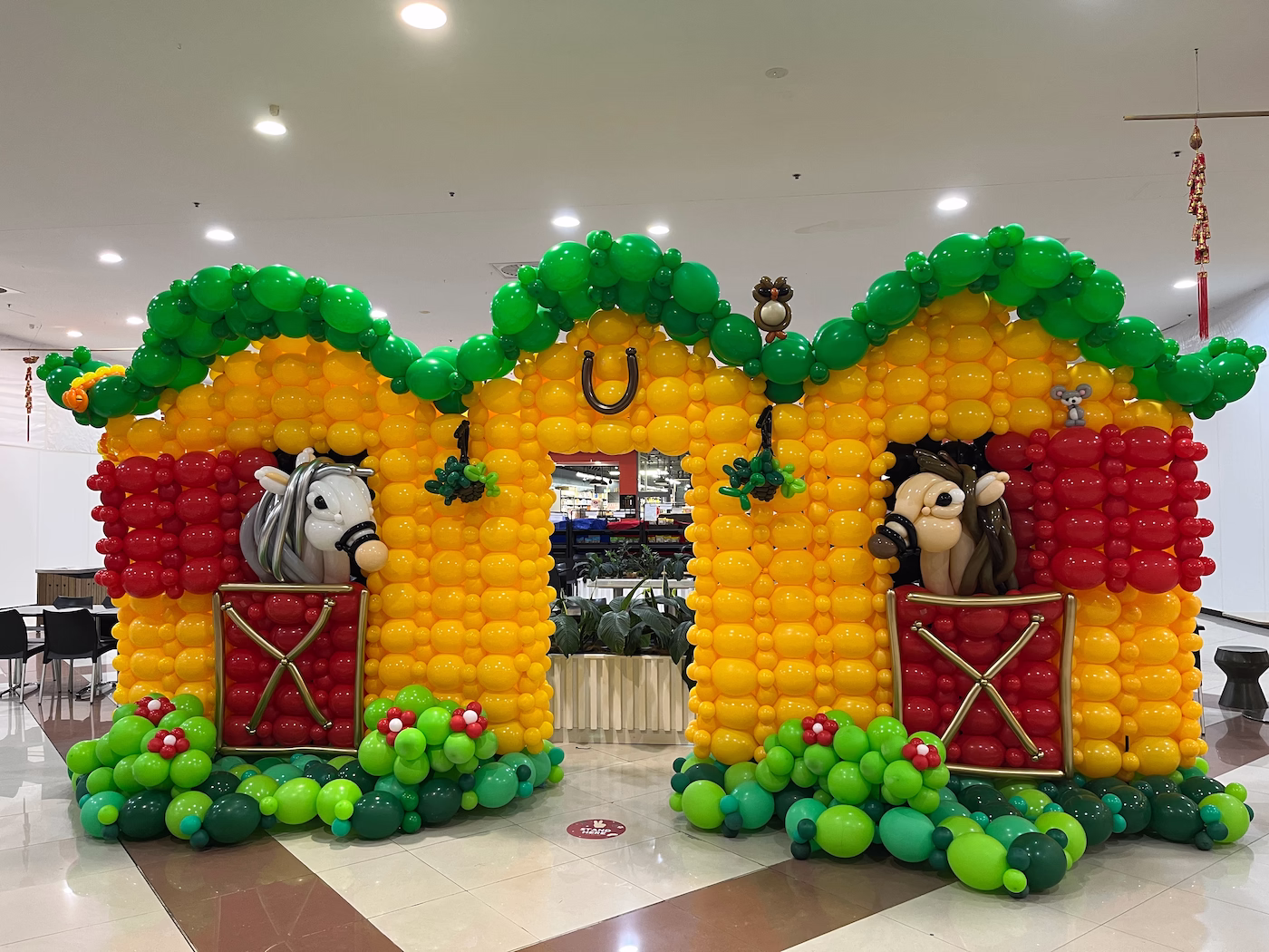 Sunny Park户外用餐区，黄红色气球马厩，绿色屋顶，马头从窗探出，气球蛇猫头鹰老鼠装饰