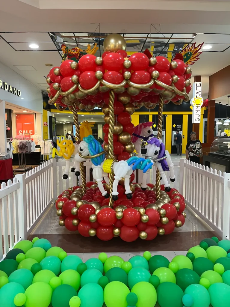 Sunnybank Plaza马年气球旋转木马，金红主色，白色马匹配蓝黄紫红鬃毛尾，绿色气球地面