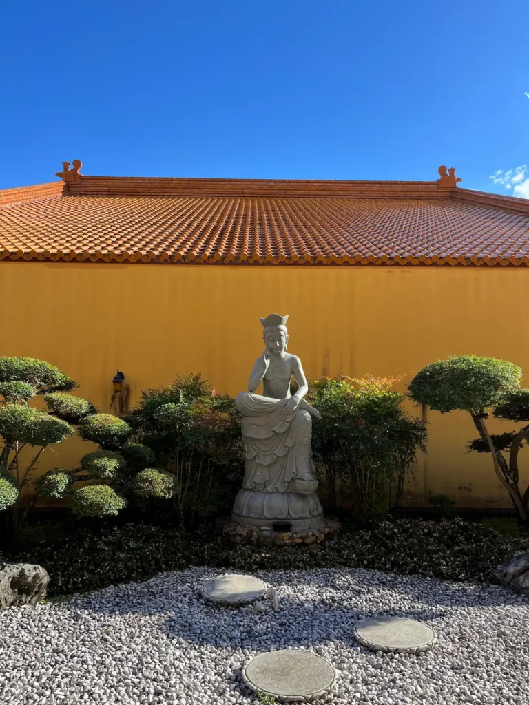 中天寺黄色院墙与黄棕色佛寺屋顶，晴朗午后天蓝，中式花园，僧侣莲花坐像，白色岩石步道