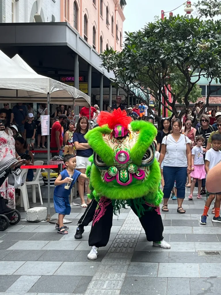 布里斯班中国城 mall，上坡街道，人群背景，绿色醒狮摆姿势，小孩伸手摸狮尾