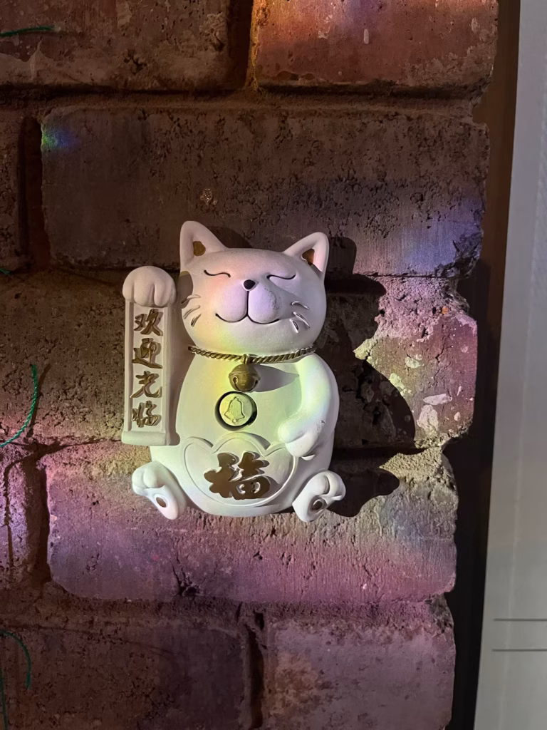 Landy's Sweet House砖墙前，日本招财猫挂饰，怀抱招牌，颈挂金铃，用作门铃
