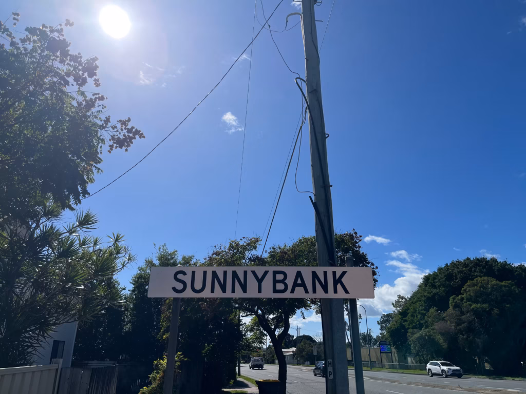 Sunnybank郊区路标，画面下方中央，远处道路车辆，左上角太阳光晕