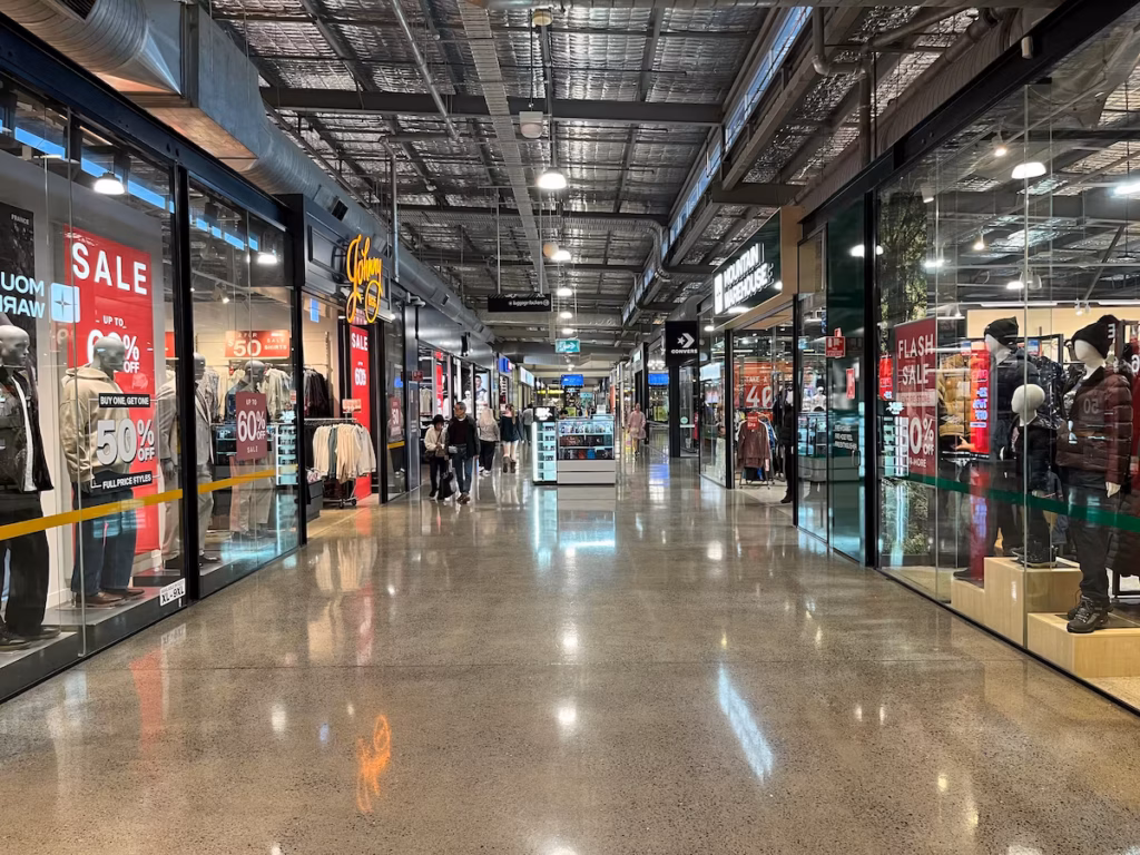 DFO内部长廊，两侧零售店，远处中央 pop-up 小摊，行人远处走动，彩色灯光，反光地面