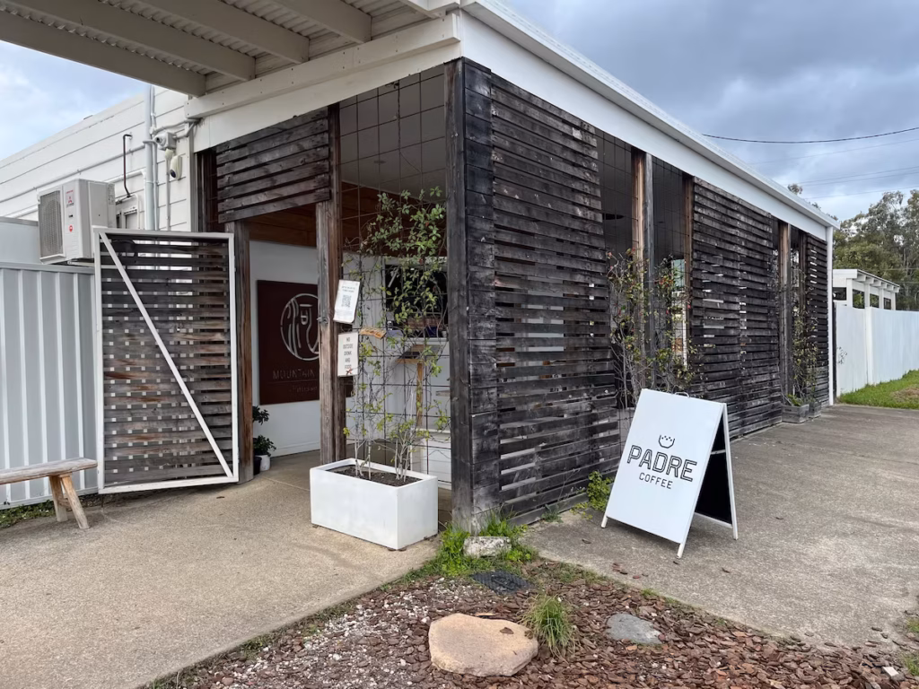 Runcorn Mango Street，Mountain River Patisserie 正面全貌，阴天，风化木外墙，暖光玻璃窗，室内人影