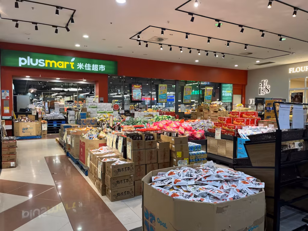Sunnypark Plus Mart 超市入口，门前堆放大宗货品与零食箱