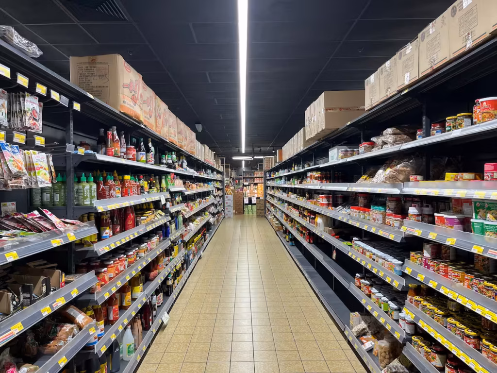 亚洲超市内部通道，两侧货架堆满食品与杂货，购物车视角
