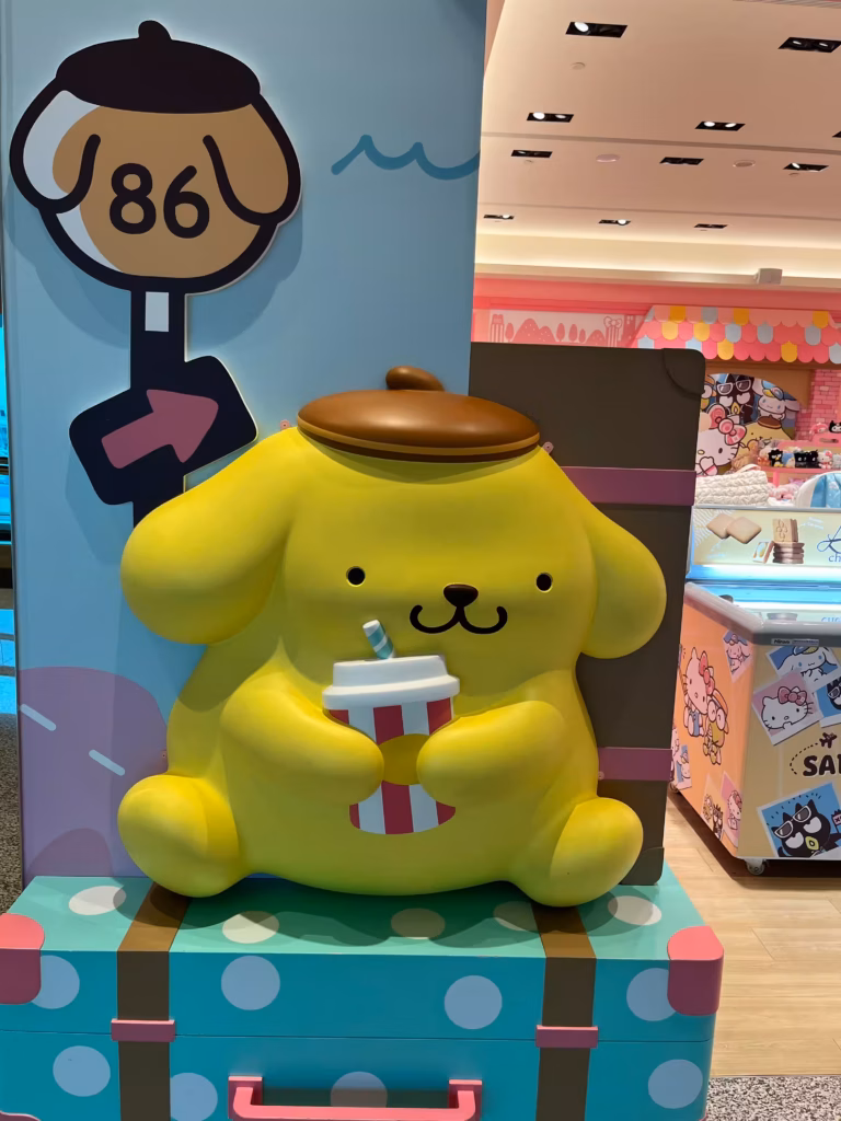 台北机场Hello Kitty商店外，布丁狗坐在蓝底白点大行李箱上，手持饮料，等待出发