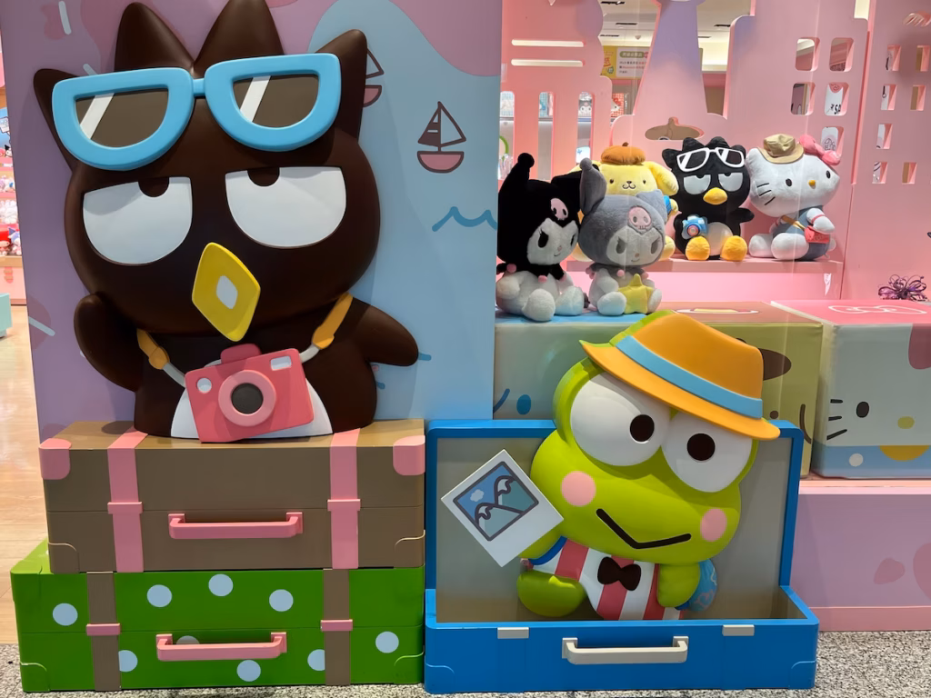 台北机场Hello Kitty商店外，Badtz-Maru颈挂粉红相机戴蓝墨镜站行李箱后挥手，Keroppi从蓝箱探出戴黄帽
