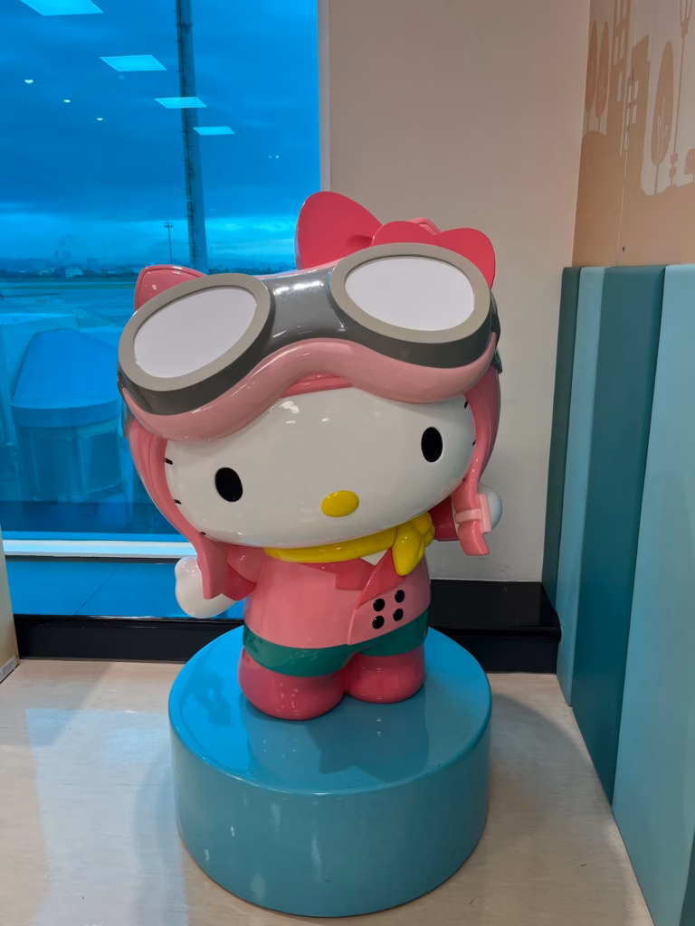 台北机场Hello Kitty登机口候机区，大型粉红Hello Kitty雕塑，身穿粉色飞行员服、黄色围巾、粉红皮帽与飞行护目镜，打卡点