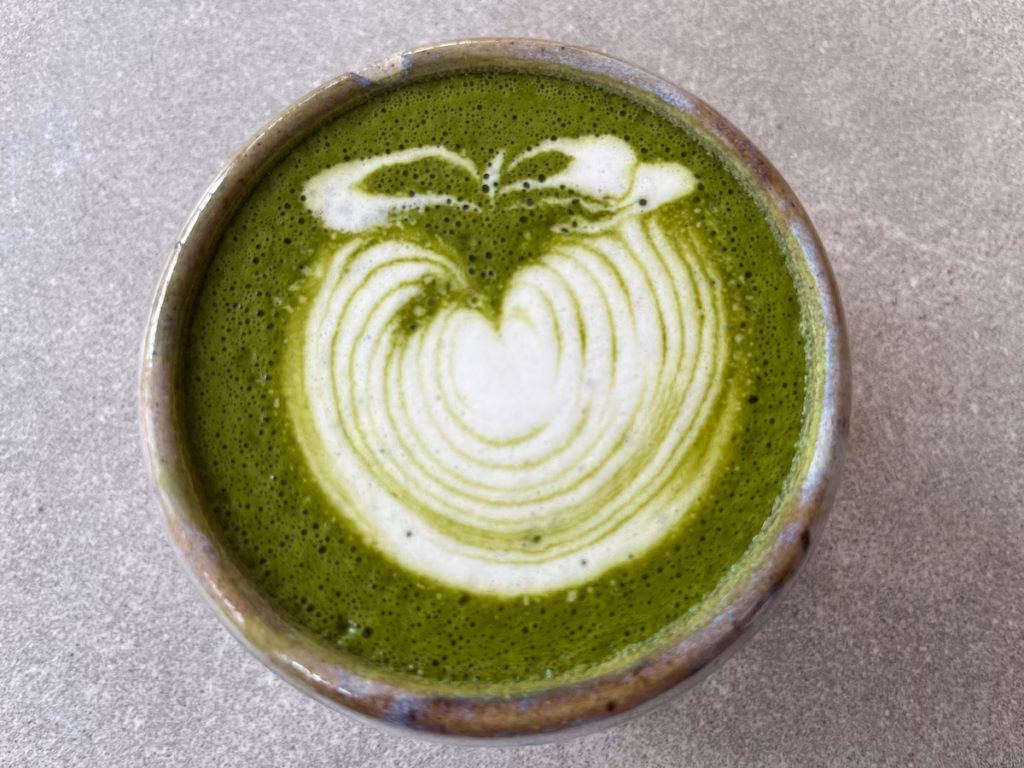 Runcorn 咖啡馆户外灰桌，俯拍，手工陶瓷杯盛抹茶拿铁，深绿抹茶泡沫，白色苹果拉花，蓝褐釉色杯沿