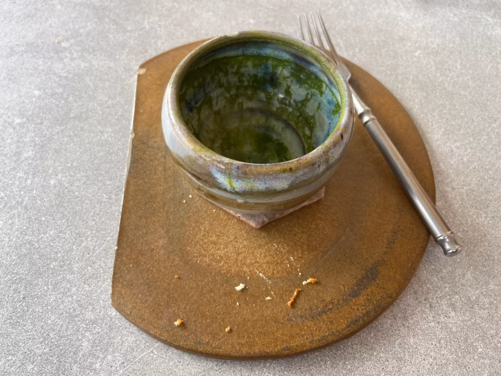 Runcorn 咖啡馆灰桌，俯拍，用过的陶瓷杯盛抹茶，旁边蜂蜜蛋糕盘有碎屑与叉，待收桌面
