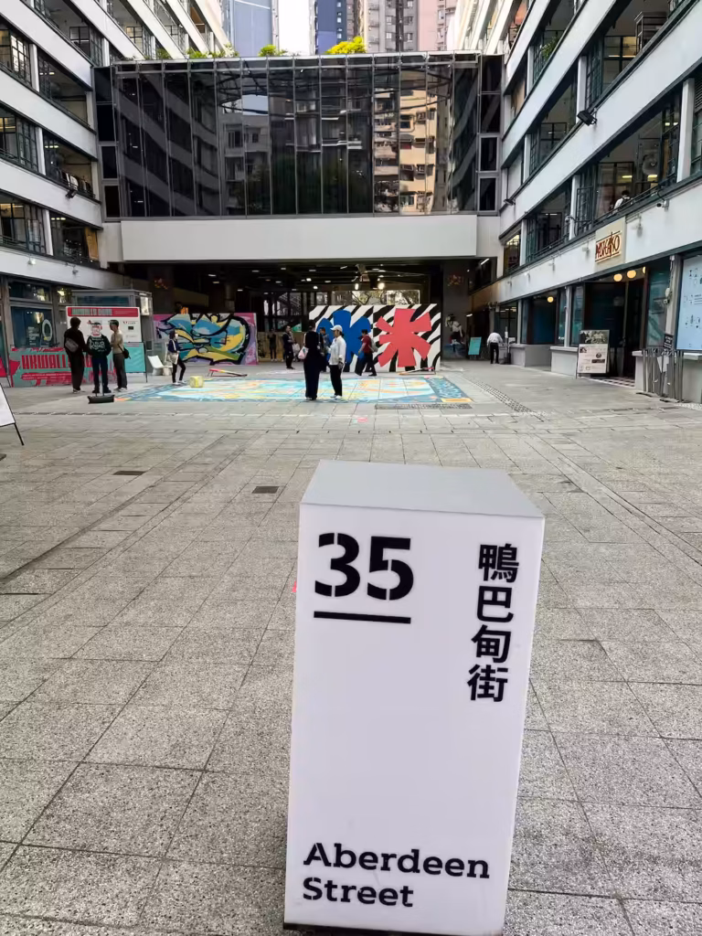 香港PMQ元创方庭院，白色方形街柱，黑色「35 Aberdeen Street」，夜间亮灯，背景街头艺术家与观众